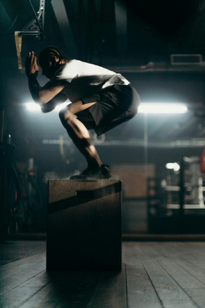 Silhouette of a man performing a box jump in a dimly lit gym, highlighting strength and agility.